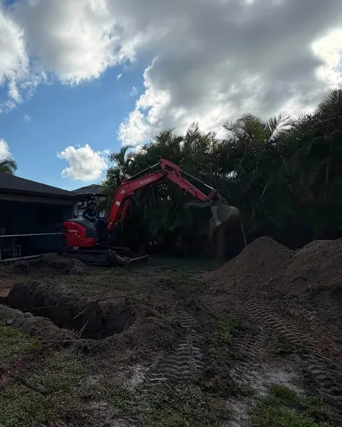 A mini excavator digging a pool hole beside a house