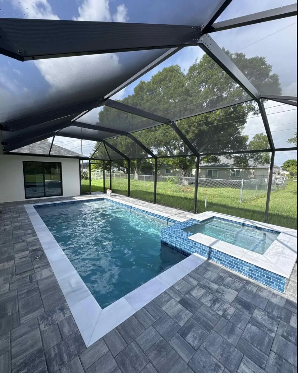 A finished in-ground pool with a tiled spa and paver deck under a screen enclosure