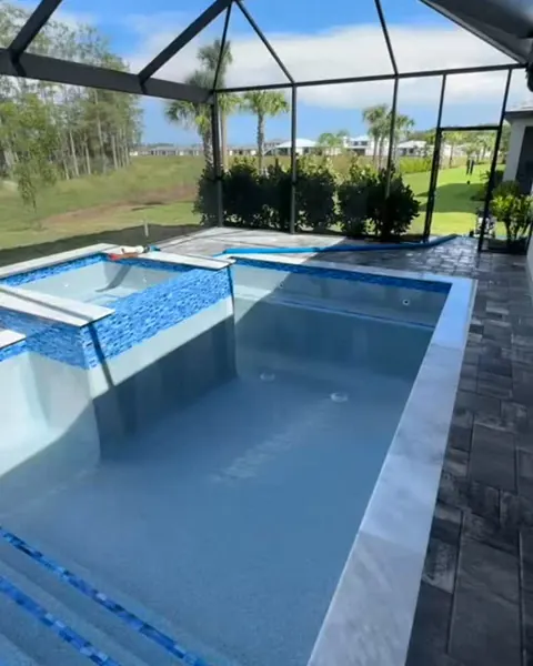 A finished pool with entry steps and a raised, tiled spa under a screen enclosure