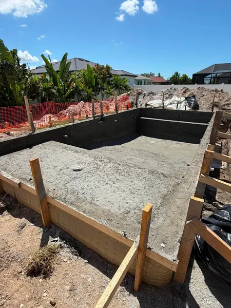 A concrete pool shell with wooden forms around the edge