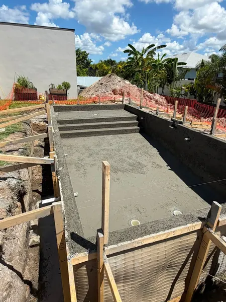 A freshly placed concrete pool shell with entry steps, still inside its forms
