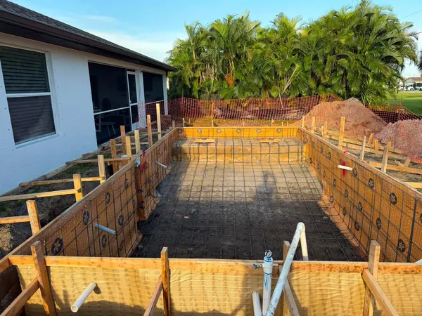 Rebar grid and wooden forms in an excavated pool beside a house